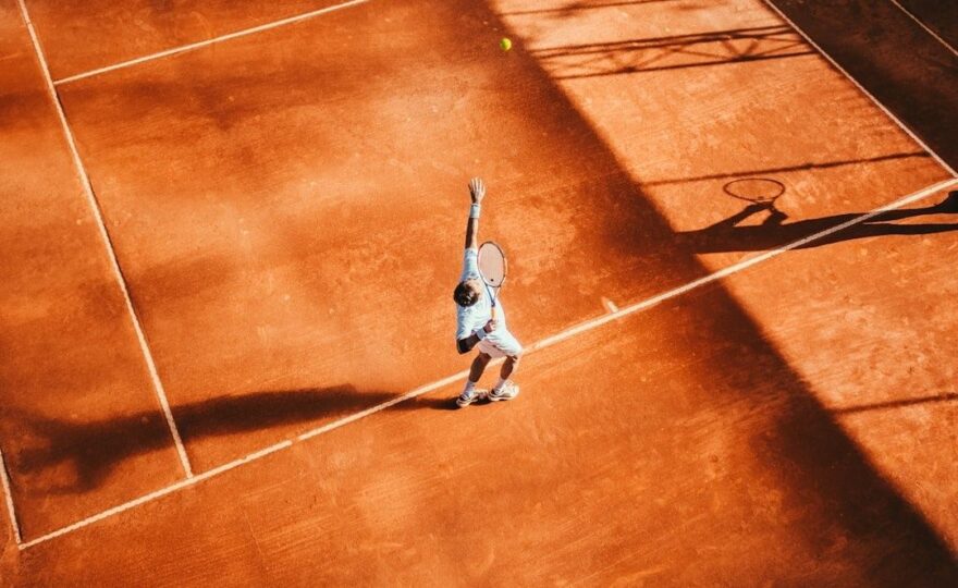 Tennisser serveert alleen op een zonovergoten gravelbaan