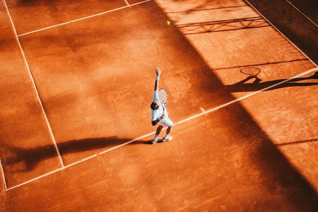 Tennisser serveert alleen op een zonovergoten gravelbaan